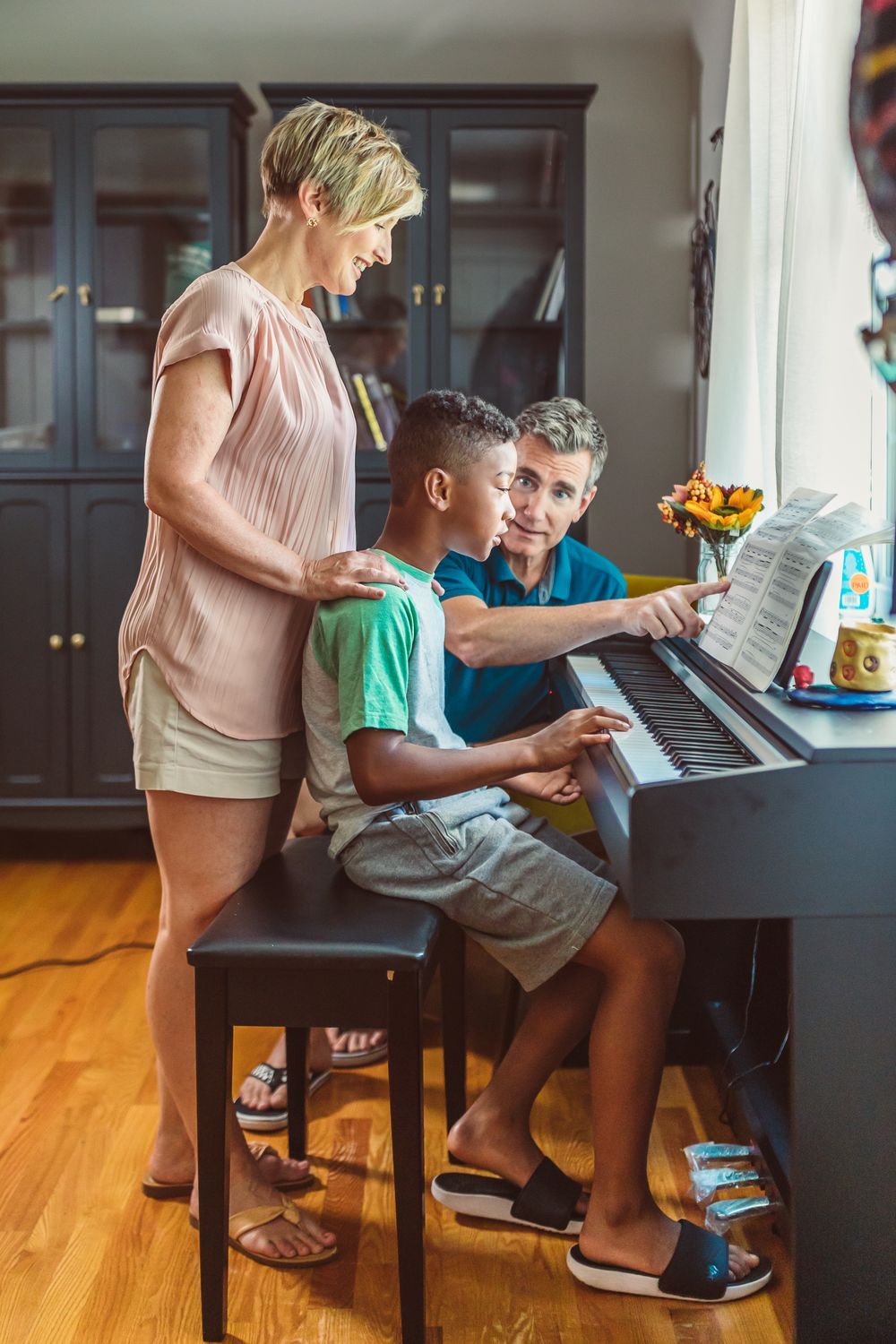 A mother guiding two children as they play piano at home